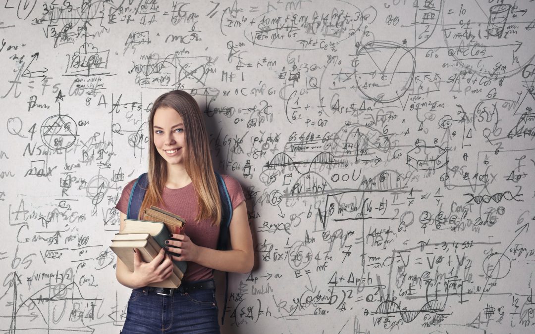 Dziewczyna z książką stojąca przed tablicą pełną wzorów
